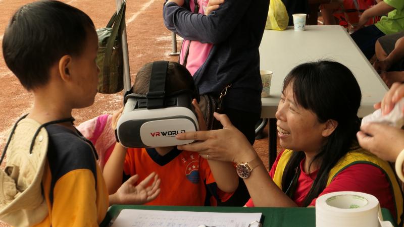 DOC的服務人員將VR眼罩放在小朋友的雙眼前，嘗試體驗擬實境的世界。