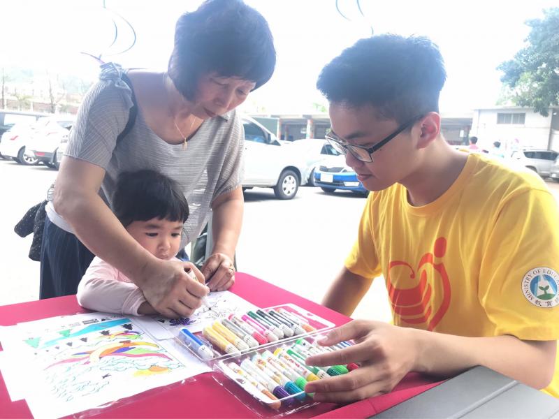 一位阿嬤握著孫女細小的手，在圖紙的空白區塊上以彩色筆填入顏色，志工人員則陪伴著他們直到離開。