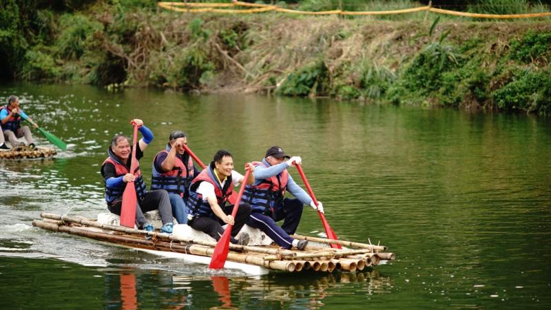 四位參賽者身穿紅色的救生衣，在阿美族的傳統竹筏上賣力地滑動船槳，後方濺起大浪的水花。
