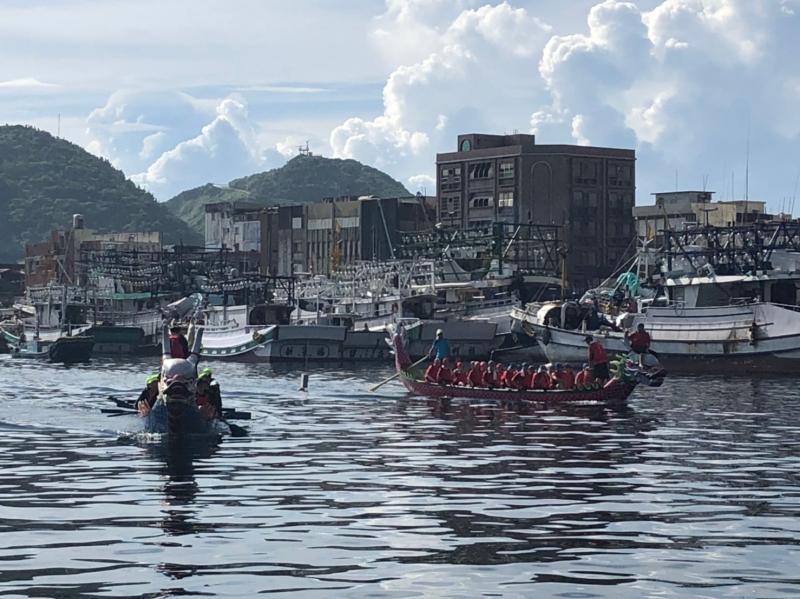 漁港的海面上除了載浮載沉的漁船外，多了兩艘滿載划龍舟參賽者的比賽選手。