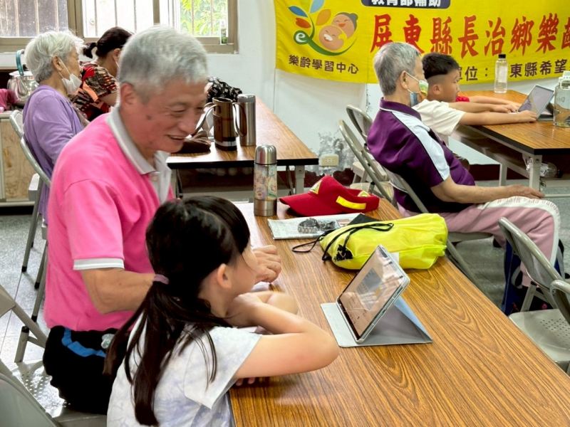 長輩與幼兒園學生搭檔學習，專注操作AI平板，笑聲中展現溫馨跨世代互動