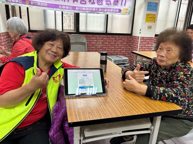 兩位女性長者開心與平板電腦上顯示闖關成功得到的高分合照並比出「讚」的手勢，看起來充滿成就感。