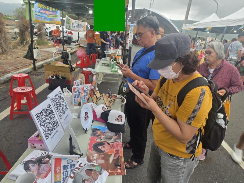 攤位陳列客製化成果並設有闖關QR Code看板，吸引長輩、家長與孩童熱烈參與，紛紛使用手機與平板認真答題。