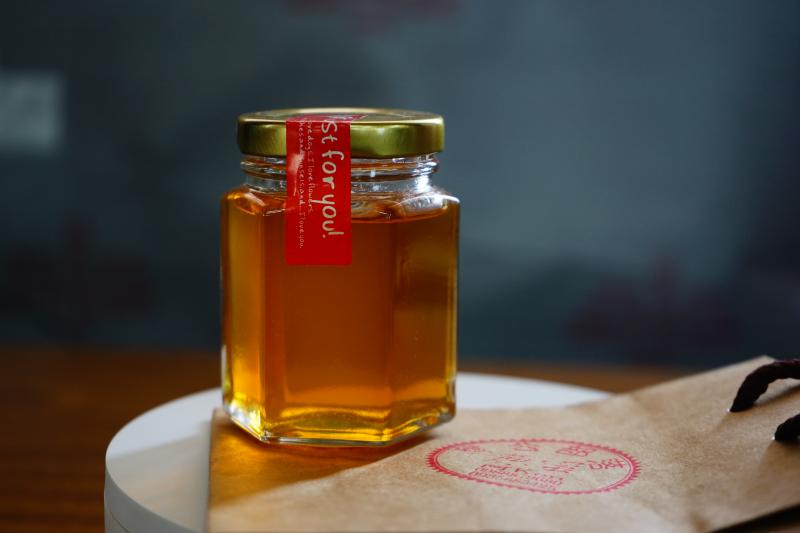 玻璃六角罐裝著琥珀色的蜂蜜，光線的照射下可以直接穿過，顯現出蜂蜜的純淨。