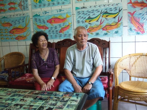 劉生根爺爺坐在自家的客廳接受，牆上掛滿自己筆下的畫作。