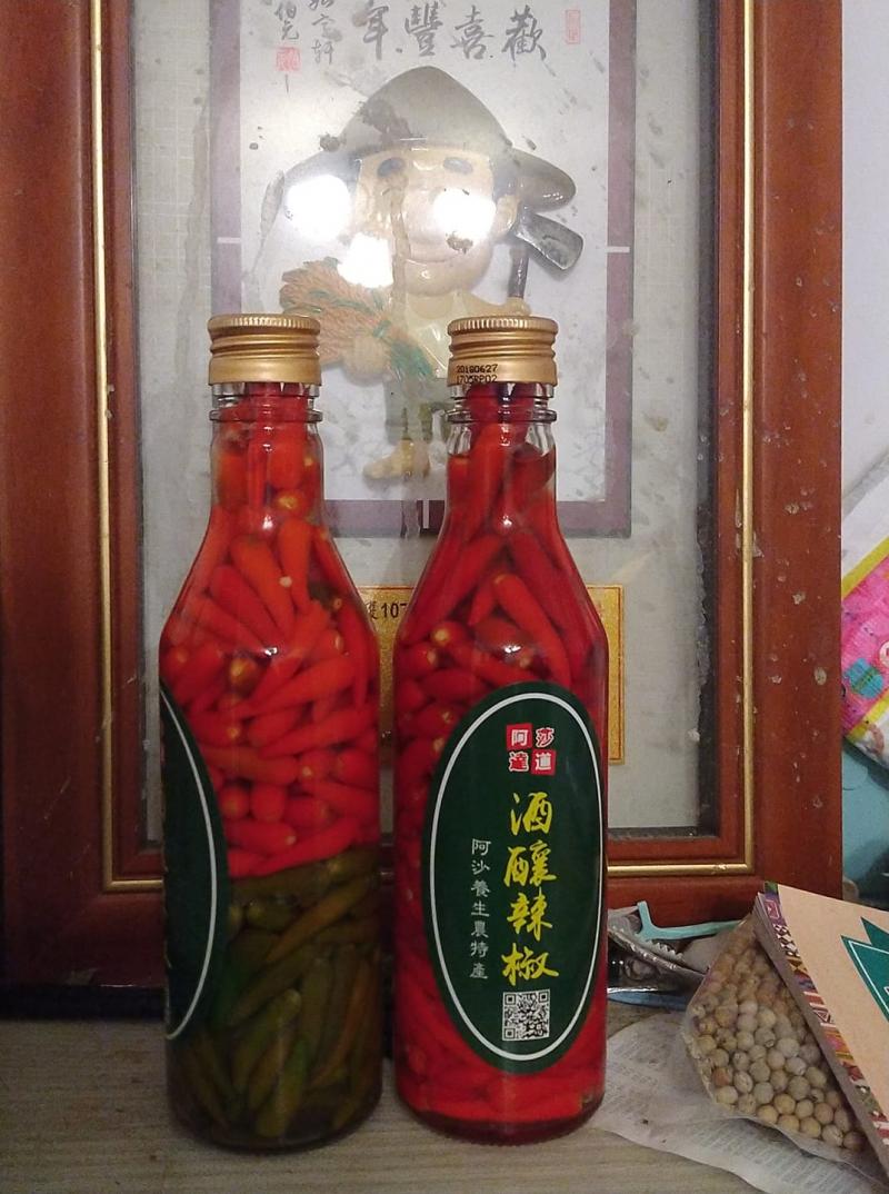 鮮紅的辣椒泡在兩瓶酒裡面，其中一瓶的底部泡著已經退色的陳年辣椒。