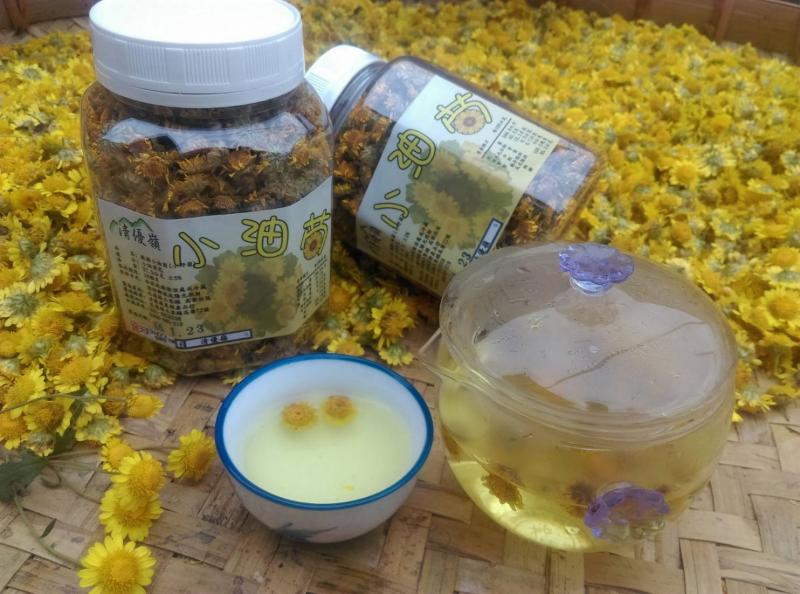 將罐裝的乾燥橘花茶與散落在桌上的菊花放在一起，一旁呈現淡黃色的菊花茶散發幽香。