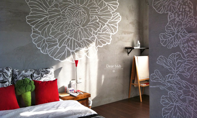 陽光藉由窗簾的縫隙透入房間，帶有歐系木造裝潢系統的氣息，牆上畫滿白底花朵點綴。