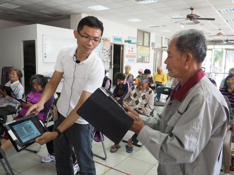 老師拿著QR code 讓里民練習掃描