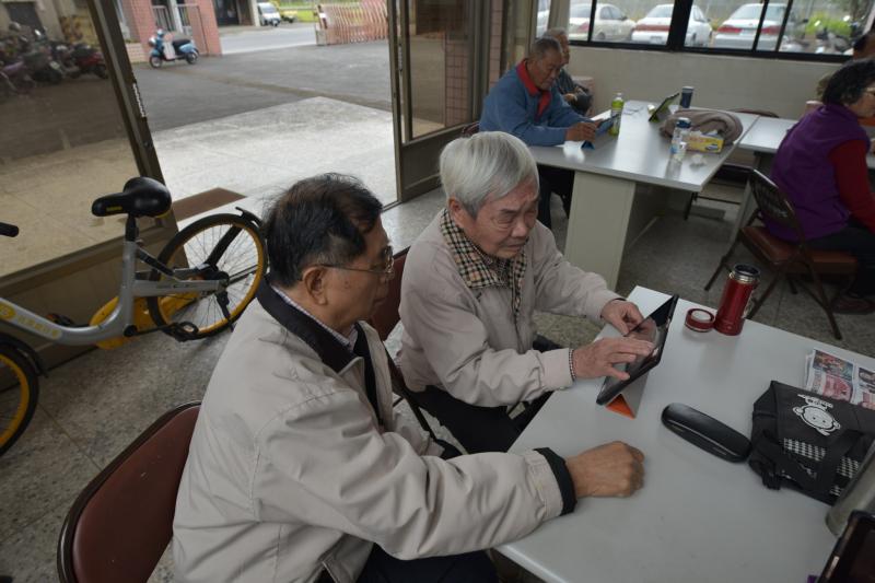 退休蕭老師協助其他高齡退休阿公操作平板電腦與手機。