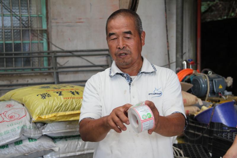 綠華有機園農場主人阿龍伯在展示農產品的認證標籤。