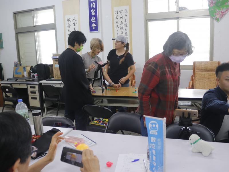 照片中陳玉薔戴著帽子與同學練習用手機操作