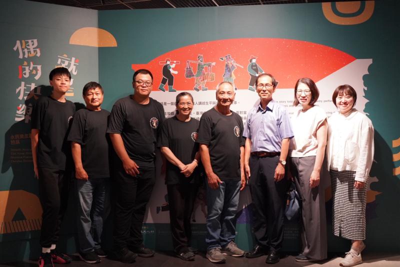 【彌陀DOC】特展入口意象合影。左起永興樂皮影劇團演師及張信鴻團長、張英嬌團長、張新國藝術總監，及高史博李文環館長(右三)、策展人劉處英老師(右二)、高巿圖彌陀公園分館主任曾雅蓮(右一)