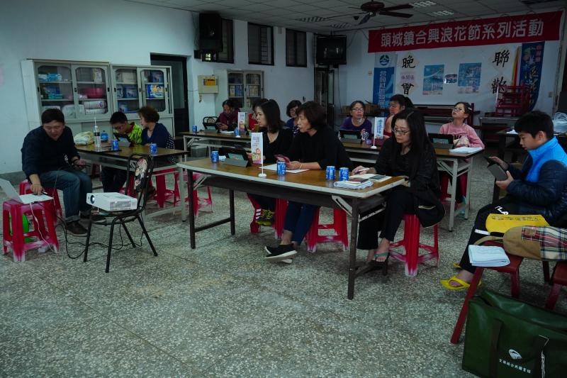 講師位於教室左方說明課程內容，學員不時頭查看授課內容，遮上同時擺放近用計畫的旗幟與飲料。