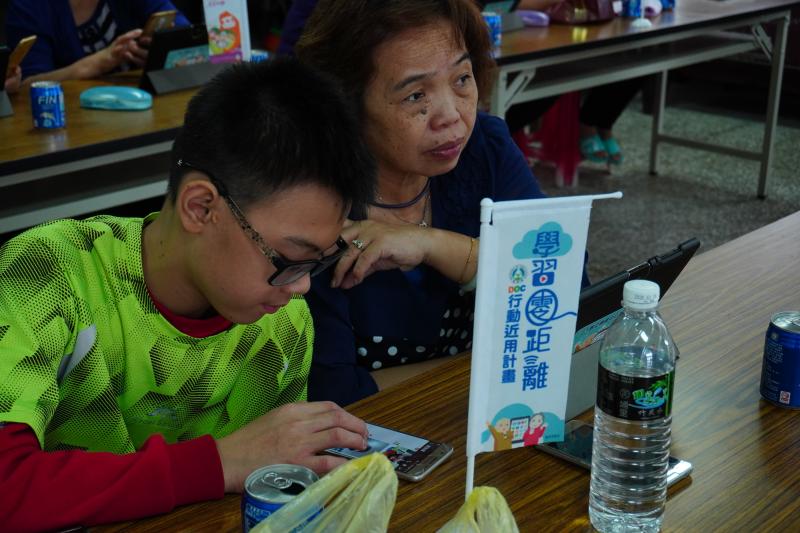 一對祖母與孫子的學員學習平板電腦的使用方式，祖母專心聽著講師的說明，孫子則以手機實際操作課程內容。