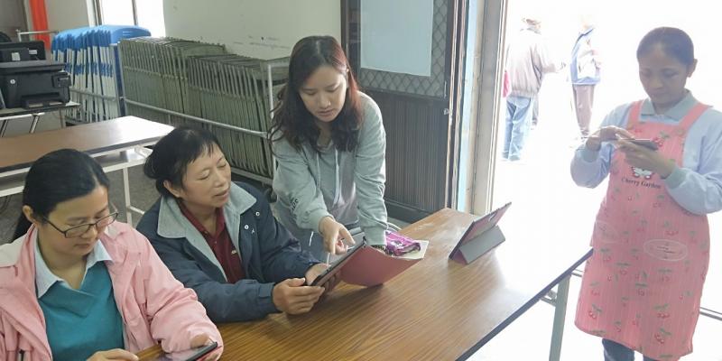 講師站在學園旁邊教導學源基礎的平板操作，學員各自操弄起自己的平板。