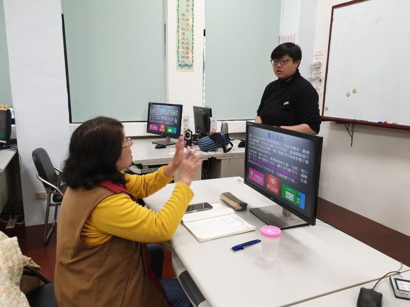 學員坐在電腦桌前，提出電子支付的設定與操作問題，配合雙手於空中比劃輔助講師了解。