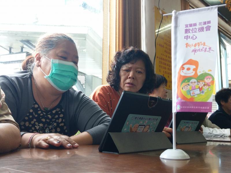 兩位長輩學員緊盯平板電腦上的畫面，左方的學員帶著綠色口罩，右方學員皺起眉頭若有所思。