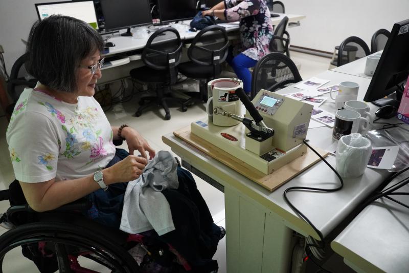 一位學員正將馬克杯放入C型模具中，嘗試以熱轉印技術將圖案烙上白色馬克杯。