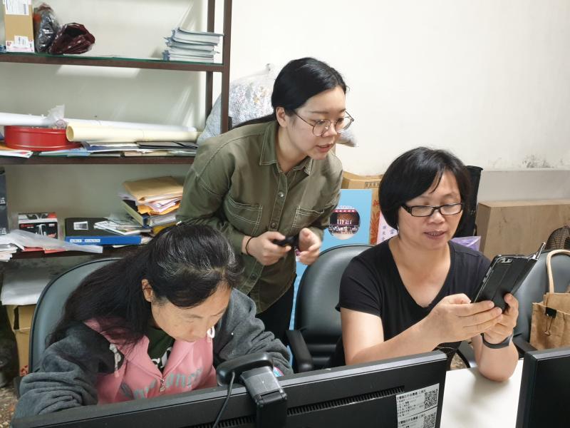 講師站在兩位學員身後指導使用製作卡片的應用程式，其中一位學員將手機拿起與講師互動。