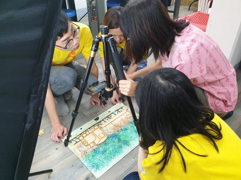 志工同學將雕刻好的火車木板模型，放置於繪製林間鐵道上，拍攝照片。