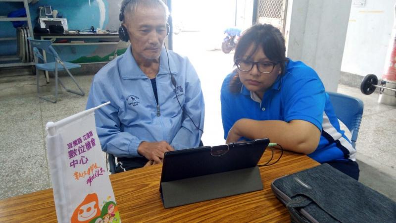 照服員在一旁協助長輩使用體驗平板的功能，兩人共同看著一台平板電腦。