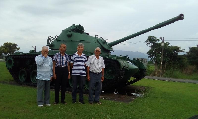 四名長輩學員站在綠色的戰車雕像前，還不忘露出笑容合照。