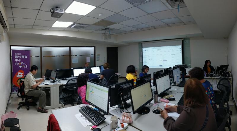 講師正於自身的電腦桌前操縱Google雲端硬碟，同時於投影幕上顯示，學員不時緊盯前方布幕。
