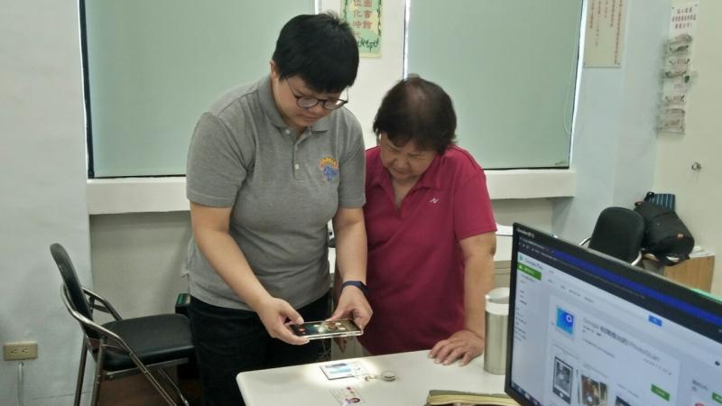 一位年輕的學員正在教導另一位年長的學員使用手機拍攝桌上的物品。
