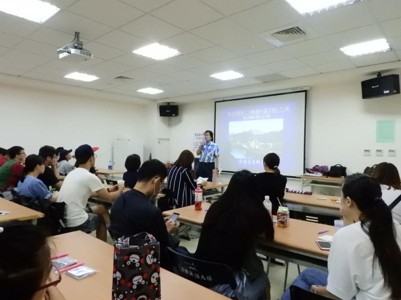 吳德亮老師站在投影布幕前面，為台下的學員說明相機的拍攝技巧及構圖方式。
