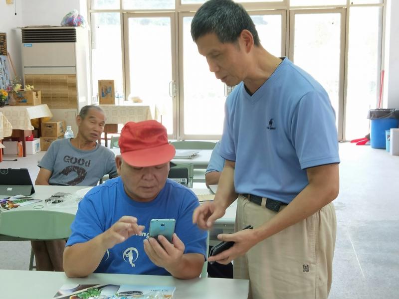 助教鄧恩隆於課堂上輔導年長的學員,從旁協助如何操作手機及平面電腦
