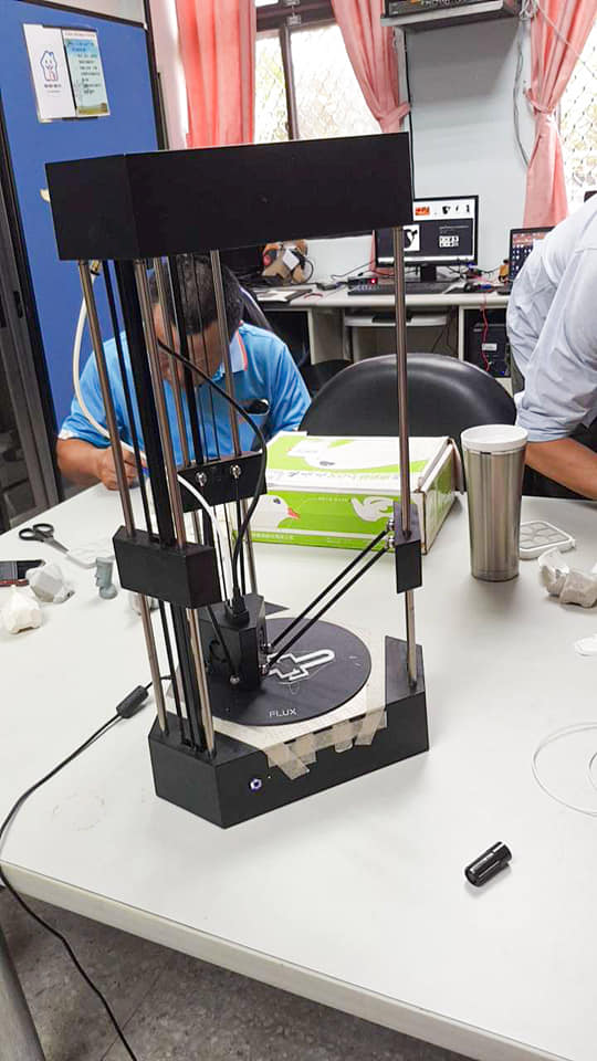 立於桌上的3D列印機，由三支柱子所支撐著，中間友會降下一快專門出料與移動的三角立方柱。