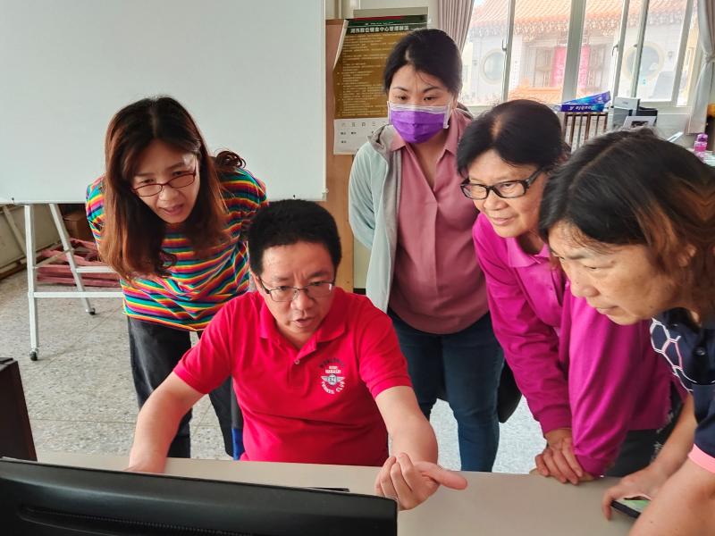 講師使用電腦示範操作，學員圍繞一旁用心觀看。