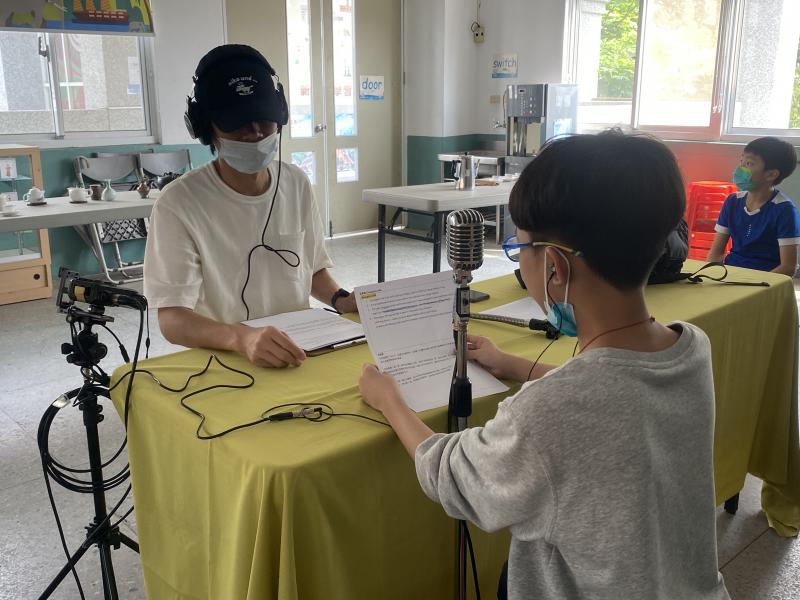 一位北埔國小同學在講師的協助下對麥克風講稿錄音