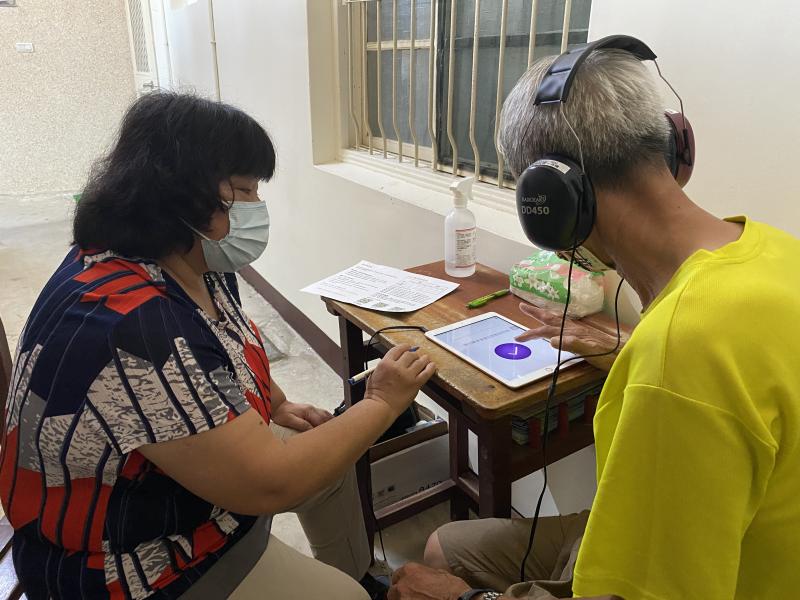 一位女性志工協助男性長者使用平板及耳機測驗聽力