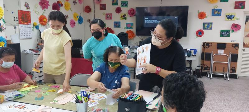 劉欣怡老師親切指導長照中心長輩描繪生活圖像，並仔細剪下。氣氛和諧又有趣。
