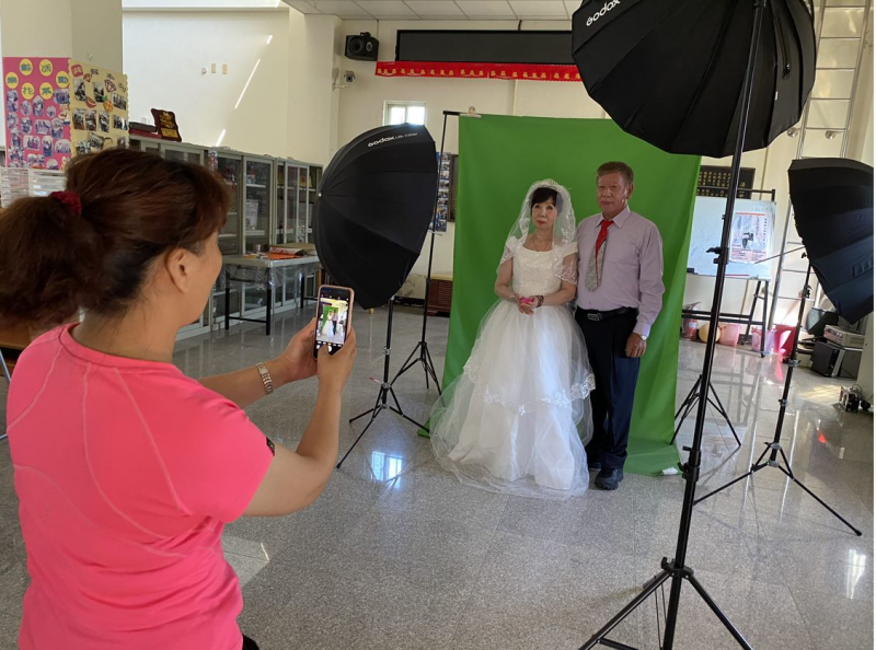 學員拿著手機，拍攝身穿禮服的老夫婦。