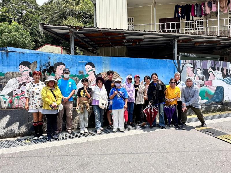 大家開心地在社區的泰雅族遷徙壁畫前合照