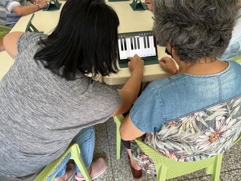 由志工協助，老太太正在用平板電腦上的應用程式自主彈奏音樂。