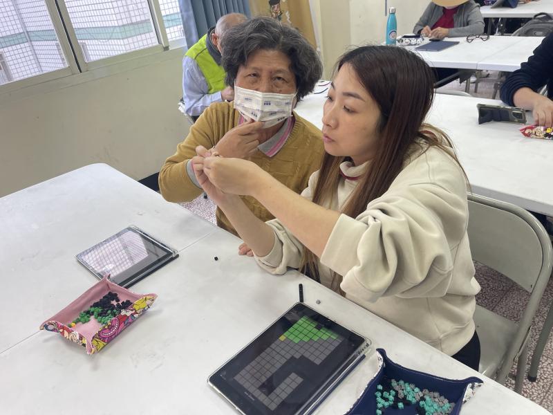 志工協助長輩將作品按圖施作在拼豆上，一共有2種作品，一是自己的創作，二是全班集體創作。