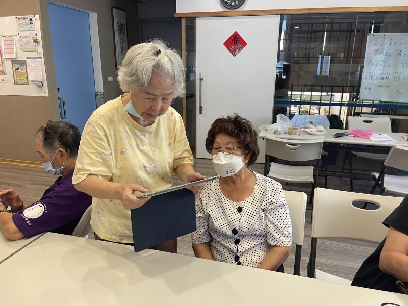 兩位女性長輩小心翼翼地握著埔里 DOC 提供的平板電腦，這是她們第一次接觸智慧裝置。認真學習的神情令人動容。