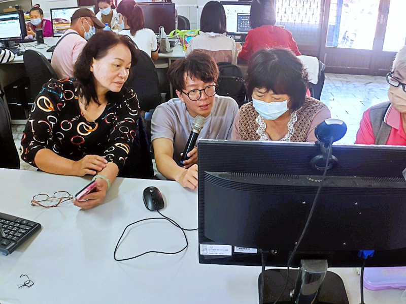 婦女網購小編班課程，講師手持麥克風於座位間指導電腦後台操作，周遭學員聚精會神共同學習。