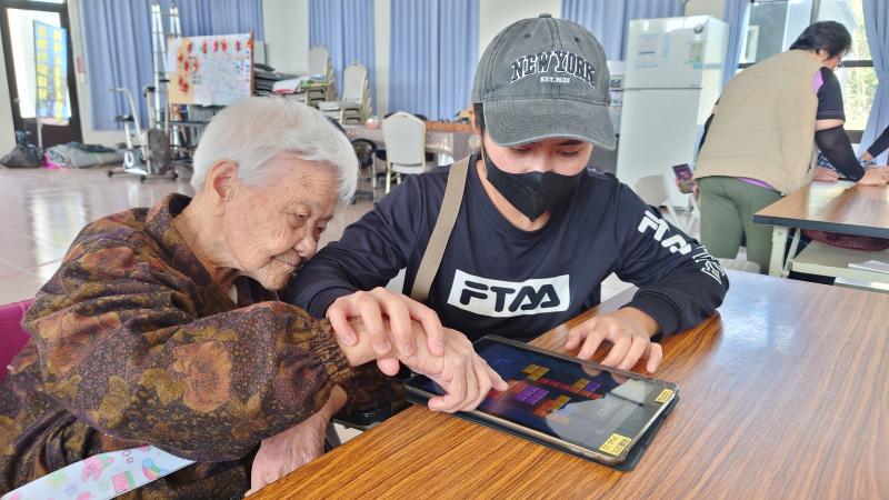 外簎看護帶著阿婆(本社區最年長者)一起玩平板,動手又動腦