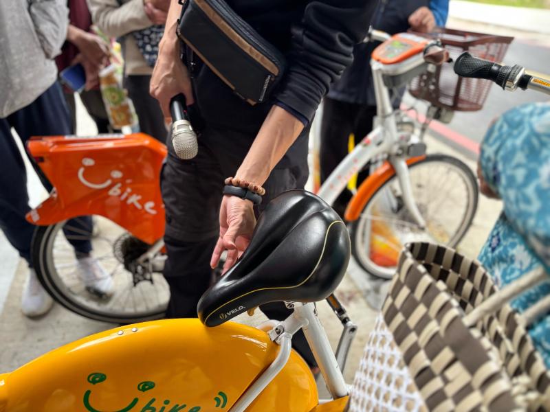 講師示範如何辨識 YouBike 公共自行車的故障狀態。講師指向車座墊並將其反轉，告訴學員這是單車待維修的表示方法。
