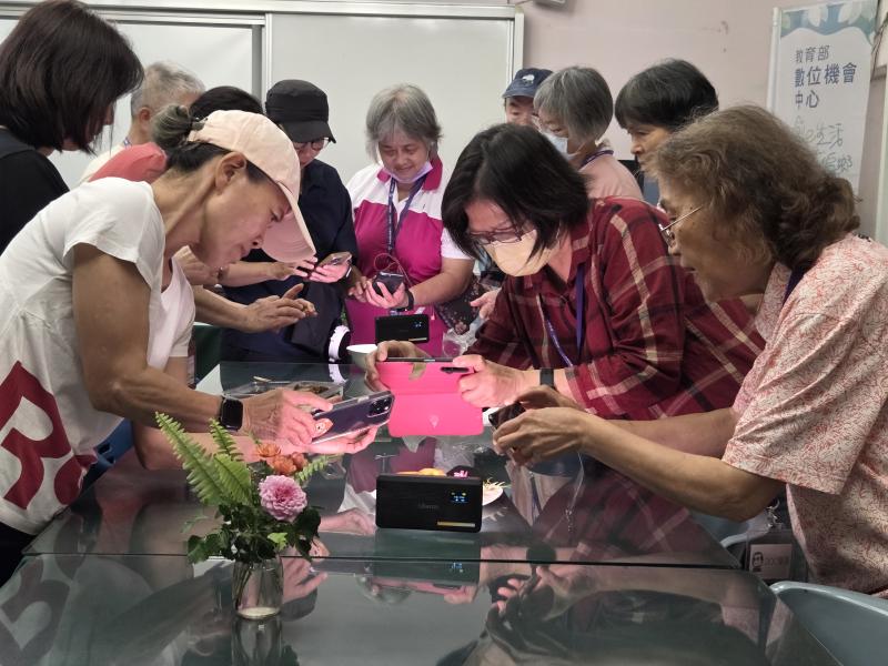 色彩獵人課程中，多位學員圍聚於桌旁，手持手機近距離拍攝桌上的玫瑰花與水果，練習手機微距攝影技巧。