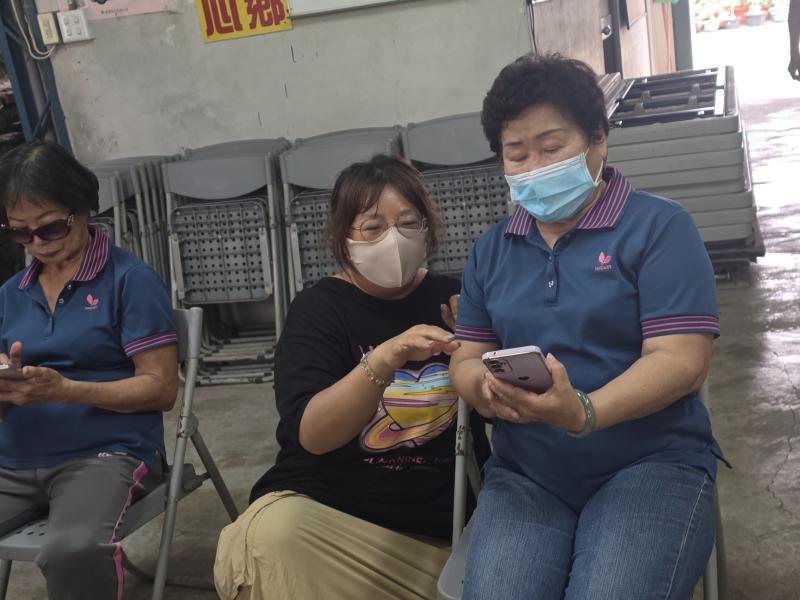 女學員與助教一同觀看並討論著手中的智慧型手機螢幕。