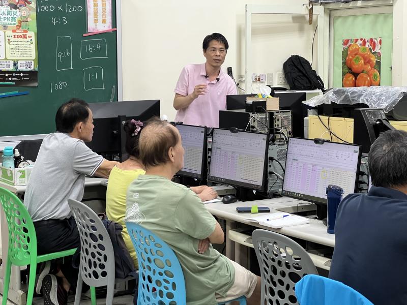 老師站立於教室前方講解,學員們圍坐電腦前專注聆聽