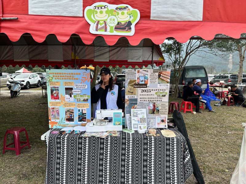 信義DOC數位學習推廣攤位,展示各類數位課程與學習應用一位工作人員熱情介紹,桌上擺放縫紉數位電繡學習成果,吸引參觀者了解如何將數位科技融入提升在地居民的數位技能.