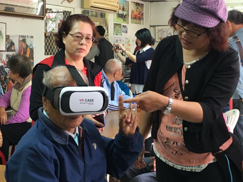 新埤DOC帶著數位設備到社區關懷據點，在志工的協助下，讓爺爺體驗虛擬實境的樂趣。