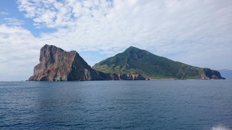 龜山島遠方側看上揚的鼻尖指向天邊的雲，位於後方的龜殼滿布綠色植被，受海浪沖刷的岩石，如四肢浮出海面。